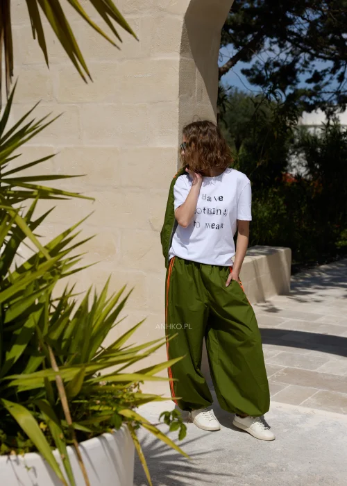 Biały T-shirt damski z nadrukiem „I Have Nothing To Wear” w czarnym kolorze. Luźny model casual zestawiony z zielonymi spodniami i okularami przeciwsłonecznymi.