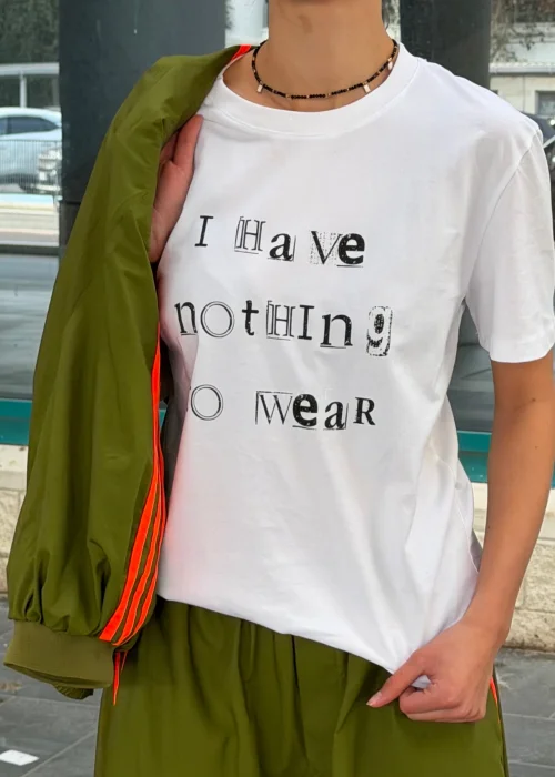 Biały T-shirt damski z nadrukiem „I Have Nothing To Wear” w czarnym kolorze. Luźny model casual zestawiony z zielonymi spodniami i okularami przeciwsłonecznymi.