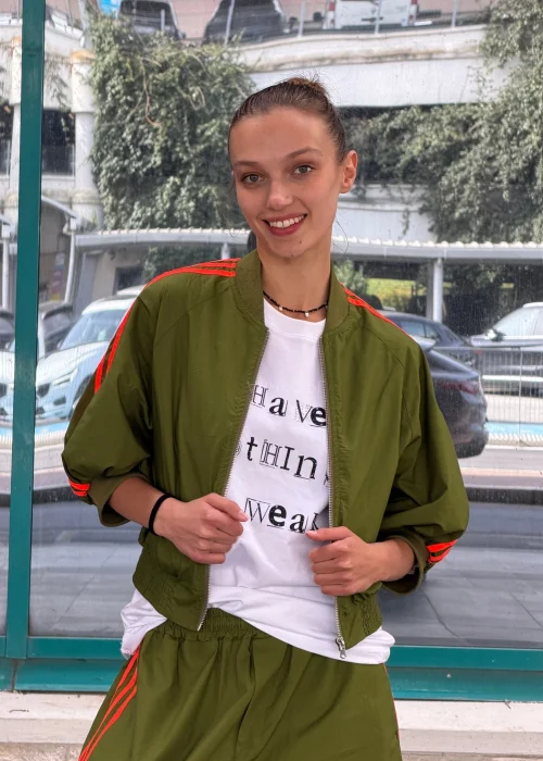 Biały T-shirt damski z nadrukiem „I Have Nothing To Wear” w czarnym kolorze. Luźny model casual zestawiony z zielonymi spodniami i okularami przeciwsłonecznymi.
