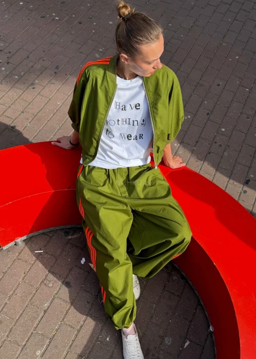 Biały T-shirt damski z nadrukiem „I Have Nothing To Wear” w czarnym kolorze. Luźny model casual zestawiony z zielonymi spodniami i okularami przeciwsłonecznymi.