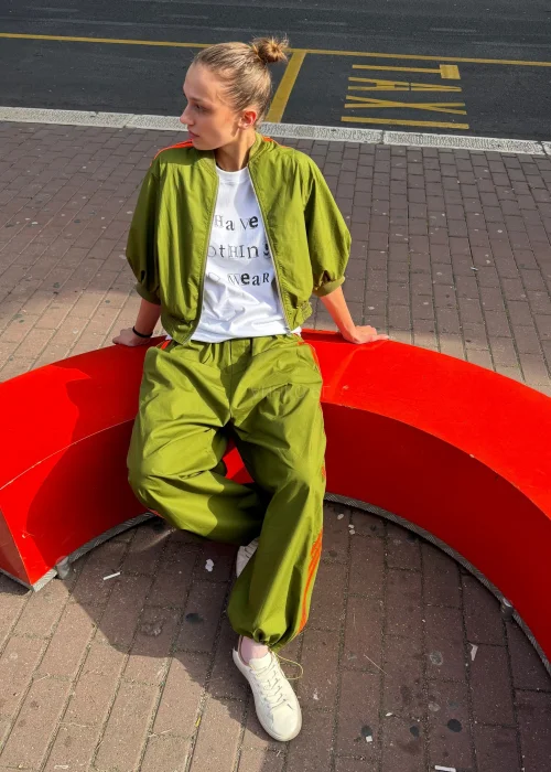 Biały T-shirt damski z nadrukiem „I Have Nothing To Wear” w czarnym kolorze. Luźny model casual zestawiony z zielonymi spodniami i okularami przeciwsłonecznymi.
