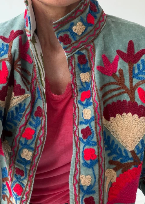 Żakiet damski w kolorze szałwiowej zieleni z bogatym haftem kwiatowym w odcieniach różu, beżu, błękitu i bordo. Artystyczny model w stylu boho z efektownymi roślinnymi zdobieniami.