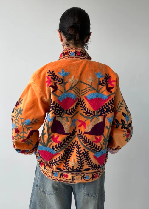 Żakiet damski w kolorze pomarańczowym z bogatym haftem kwiatowym w odcieniach różu, błękitu, granatu i beżu. Artystyczny model w stylu boho z efektownymi roślinnymi zdobieniam.
