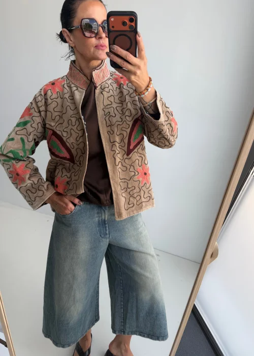 Żakiet damski w kolorze kremowego beżu z dekoracyjnym haftem kwiatowym oraz motywem motyla w odcieniach różu, zieleni i bordo. Artystyczny model w stylu boho z oryginalnym wzorem.