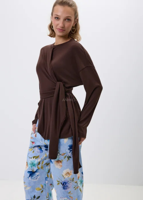 Brązowa bluzka z efektownym wiązaniem w talii i luźnym fasonem oversize. Model z długim rękawem oraz asymetrycznym drapowaniem podkreśla sylwetkę i tworzy elegancką, kobiecą stylizację.