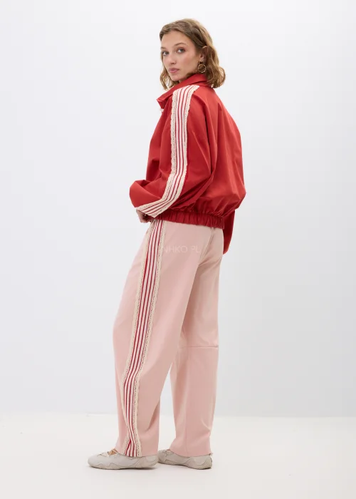 Różowe spodnie damskie z szeroką nogawką, ozdobione kontrastowymi lampasami i koronkowym wykończeniem po bokach. Komfortowy fason z elastycznym pasem łączy wygodę z modnym, sportowo-eleganckim stylem.