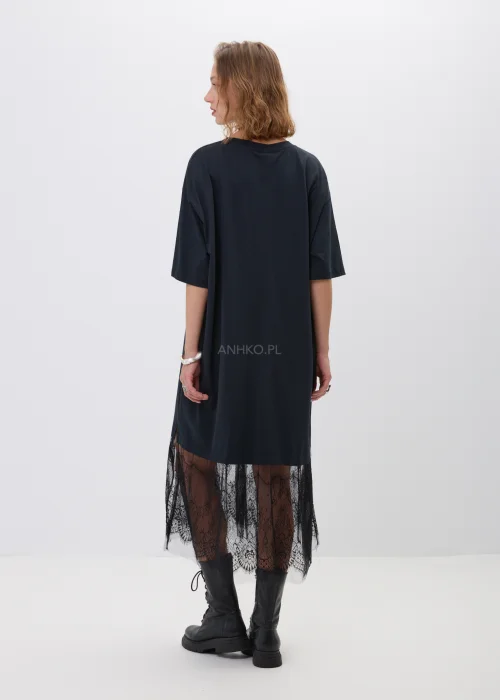 Czarna sukienka oversize z kontrastowym napisem i koronkową wstawką przy dolnej krawędzi. Luźny fason z krótkim rękawem i długością midi tworzy nowoczesną stylizację w miejskim stylu z ciężkimi botkami.