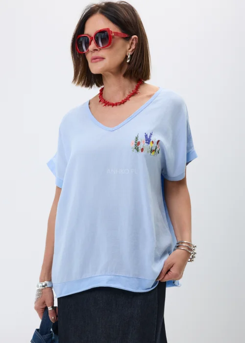 Bluzka w kolorze baby blue z dekoltem V i subtelnym haftem kwiatowym na piersi. Luźny fason oversize z krótkim rękawem nadaje stylizacji lekkości i doskonale komponuje się z jeansowymi oraz casualowymi zestawami.