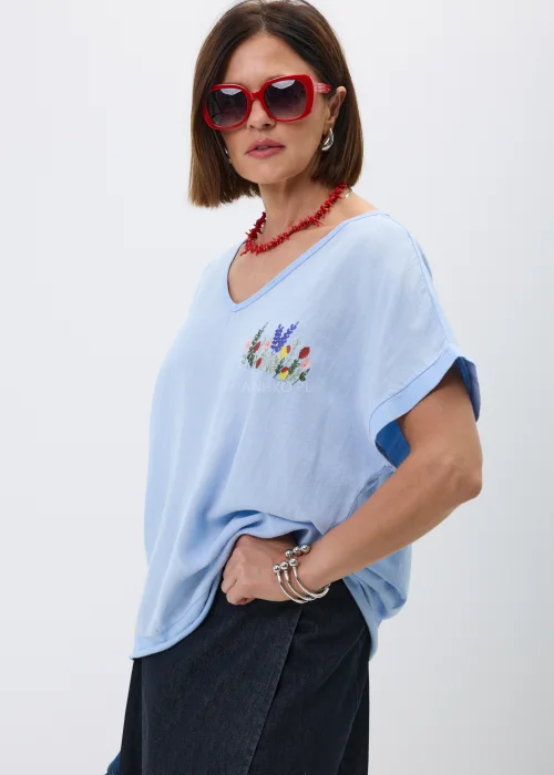 Bluzka w kolorze baby blue z dekoltem V i subtelnym haftem kwiatowym na piersi. Luźny fason oversize z krótkim rękawem nadaje stylizacji lekkości i doskonale komponuje się z jeansowymi oraz casualowymi zestawami.