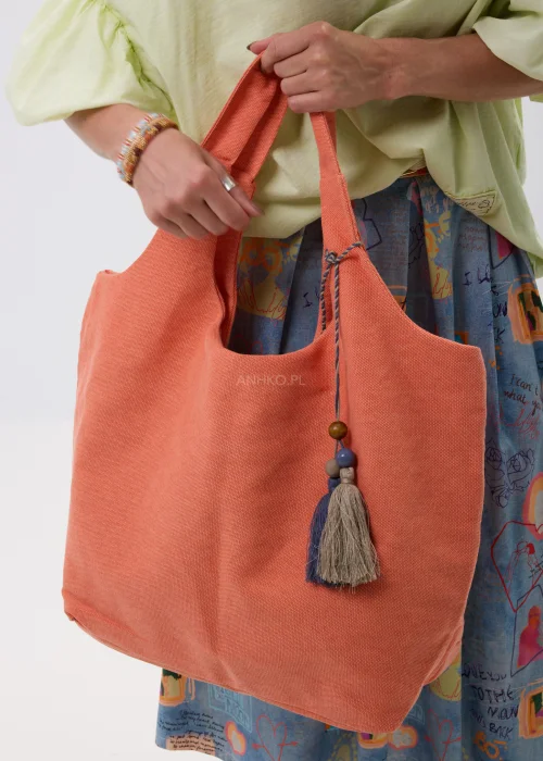 Duża materiałowa torebka shopper w koralowym kolorze z ozdobnymi chwostami i drewnianymi koralikami. Lekki, pojemny model idealny na co dzień, wakacyjne wyjazdy i swobodne stylizacje w stylu boho.