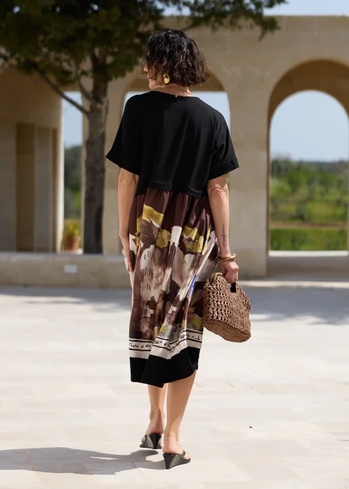 Czarna sukienka midi z artystycznym nadrukiem w odcieniach brązu i beżu, o luźnym fasonie z krótkim rękawem i praktycznymi kieszeniami, prezentowana w eleganckiej letniej stylizacji.