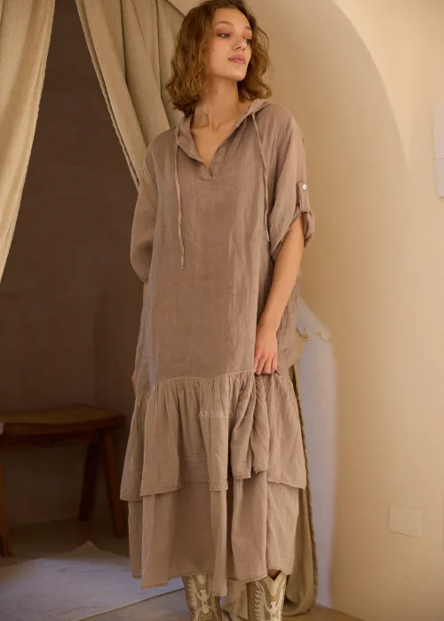 Lniana sukienka maxi z kapturem w odcieniu taupe, z dekoracyjną falbaną u dołu i podwijanymi rękawami. Swobodny fason w stylu boho doskonale sprawdzi się w naturalnych, codziennych i eleganckich stylizacjach.