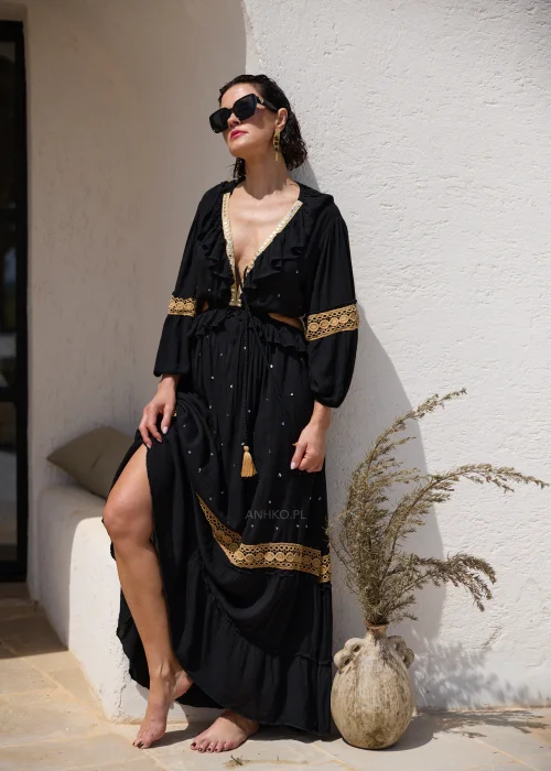 Czarna sukienka maxi w stylu boho z ażurowymi zdobieniami w kolorze złota, głębokim dekoltem V i wycięciami w talii. Zwiewny model z szerokimi rękawami i ozdobnym wiązaniem z chwostami, idealny na wakacyjne i wieczorowe stylizacje.