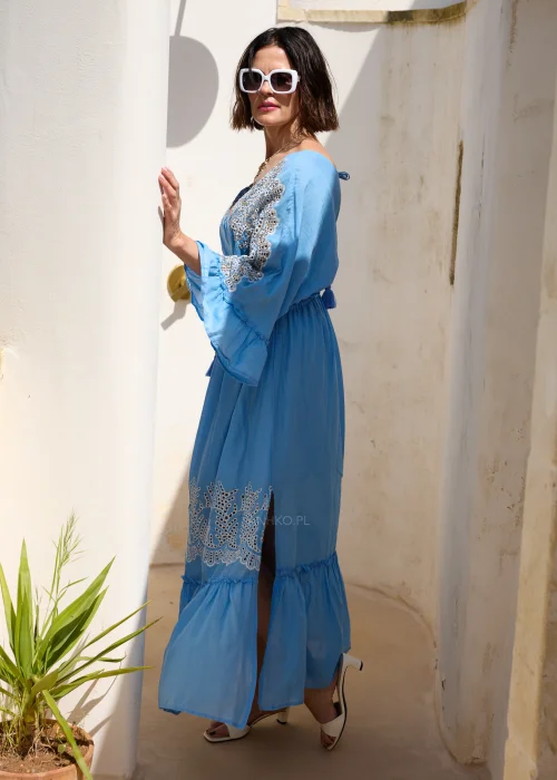 Błękitna sukienka maxi w stylu boho z koronkowymi zdobieniami, dekoltem V i wiązaniem w talii z chwostami. Zwiewny model z szerokimi rękawami, idealny do wakacyjnych i eleganckich stylizacji.