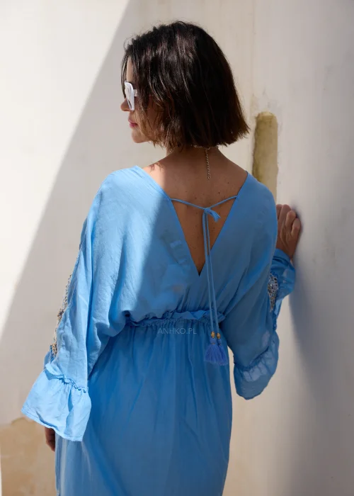Błękitna sukienka maxi w stylu boho z koronkowymi zdobieniami, dekoltem V i wiązaniem w talii z chwostami. Zwiewny model z szerokimi rękawami, idealny do wakacyjnych i eleganckich stylizacji.