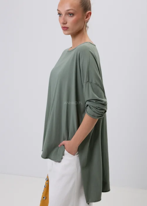 Oliwkowa damska bluzka oversize z długim rękawem i asymetrycznym dołem, wykonana z miękkiej dzianiny. Minimalistyczna stylizacja casual z białymi spodniami, idealna na co dzień i do nowoczesnych zestawów.