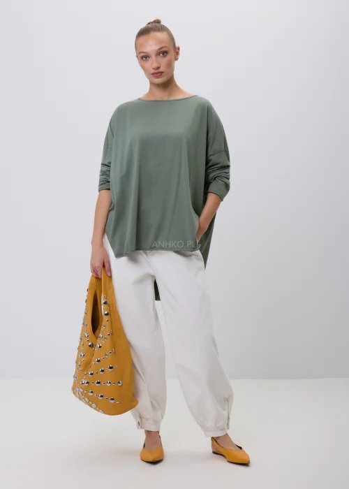Oliwkowa damska bluzka oversize z długim rękawem i asymetrycznym dołem, wykonana z miękkiej dzianiny. Minimalistyczna stylizacja casual z białymi spodniami, idealna na co dzień i do nowoczesnych zestawów.