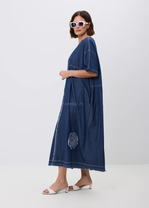 Jeansowa sukienka maxi oversize z krótkim, szerokim rękawem, ozdobiona dekoracyjnymi przeszyciami oraz naszywanymi aplikacjami w kształcie okręgów z postrzępionym wykończeniem. Luźny fason zapewnia wygodę i tworzy nowoczesną, casualową stylizację.