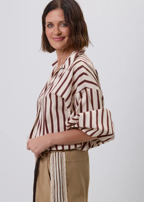 Damska koszula w beżowo-brązowe pionowe paski z kołnierzykiem i podwijanymi rękawami. Elegancka stylizacja casual ze spodniami w odcieniu camel i ozdobnym plecionym paskiem.