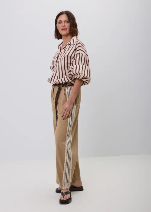 Damska koszula w beżowo-brązowe pionowe paski z kołnierzykiem i podwijanymi rękawami. Elegancka stylizacja casual ze spodniami w odcieniu camel i ozdobnym plecionym paskiem.