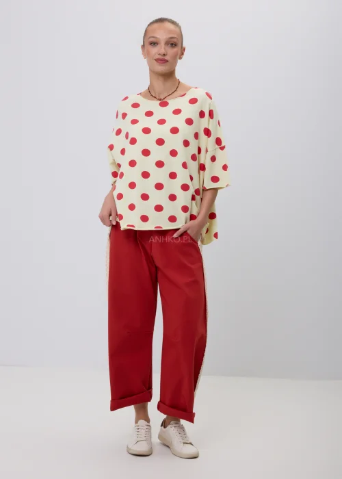 Kremowa damska bluzka oversize w czerwone grochy z rękawem 3/4, zestawiona z czerwonymi spodniami z koronkowym lampasem. Modna stylizacja casual inspirowana stylem retro i francuską elegancją.