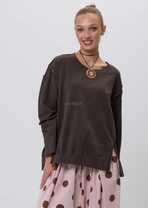Brązowa bluza damska oversize z długim rękawem i okrągłym dekoltem, o swobodnym fasonie z ozdobnymi przeszyciami. Casualowa stylizacja z szerokimi spodniami w grochy podkreśla wygodny i nowoczesny charakter modelu.