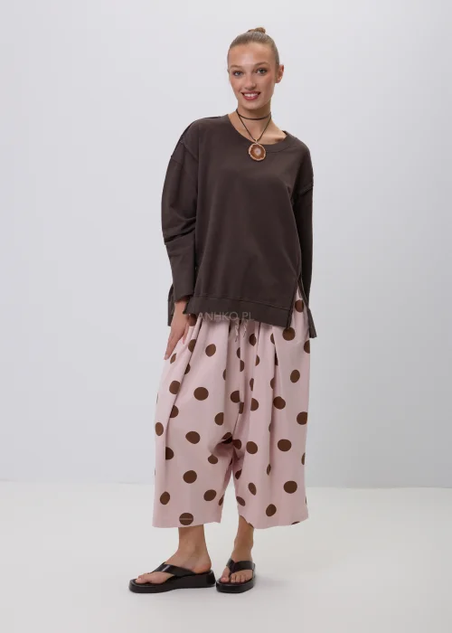 Brązowa bluza damska oversize z długim rękawem i okrągłym dekoltem, o swobodnym fasonie z ozdobnymi przeszyciami. Casualowa stylizacja z szerokimi spodniami w grochy podkreśla wygodny i nowoczesny charakter modelu.
