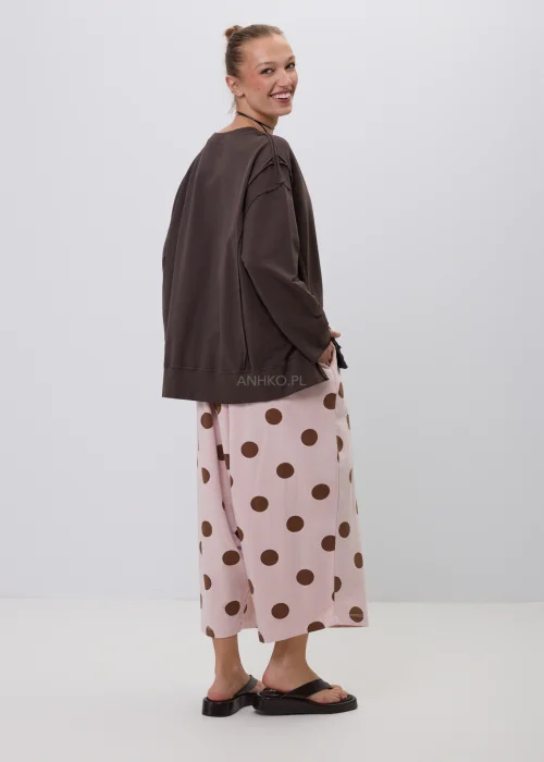 Brązowa bluza damska oversize z długim rękawem i okrągłym dekoltem, o swobodnym fasonie z ozdobnymi przeszyciami. Casualowa stylizacja z szerokimi spodniami w grochy podkreśla wygodny i nowoczesny charakter modelu.