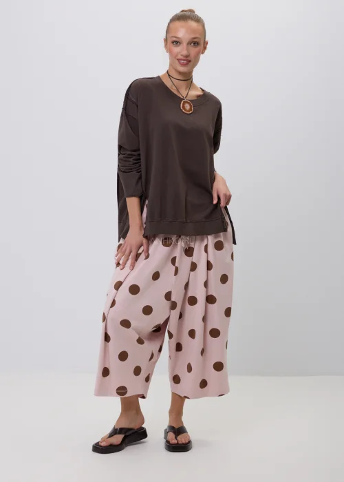 Brązowa bluza damska oversize z długim rękawem i okrągłym dekoltem, o swobodnym fasonie z ozdobnymi przeszyciami. Casualowa stylizacja z szerokimi spodniami w grochy podkreśla wygodny i nowoczesny charakter modelu.