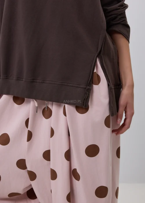 Brązowa bluza damska oversize z długim rękawem i okrągłym dekoltem, o swobodnym fasonie z ozdobnymi przeszyciami. Casualowa stylizacja z szerokimi spodniami w grochy podkreśla wygodny i nowoczesny charakter modelu.