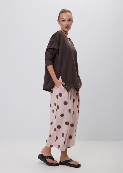 Pudroworóżowe szerokie spodnie damskie culotte w duże brązowe grochy z elastycznym pasem i luźnym fasonem. Wygodny model doskonale sprawdza się w codziennych stylizacjach o modnym, casualowym charakterze.