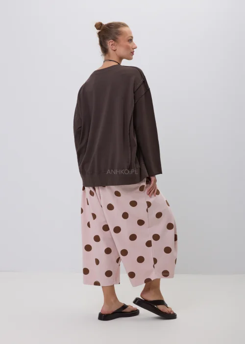 Pudroworóżowe szerokie spodnie damskie culotte w duże brązowe grochy z elastycznym pasem i luźnym fasonem. Wygodny model doskonale sprawdza się w codziennych stylizacjach o modnym, casualowym charakterze.