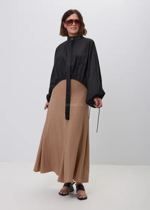 Czarna damska kurtka bomber oversize ze stójką, szerokimi rękawami i regulowanymi troczkami przy mankietach. Nowoczeska stylizacja casual z krótką kurtką i beżową spódnicą maxi.