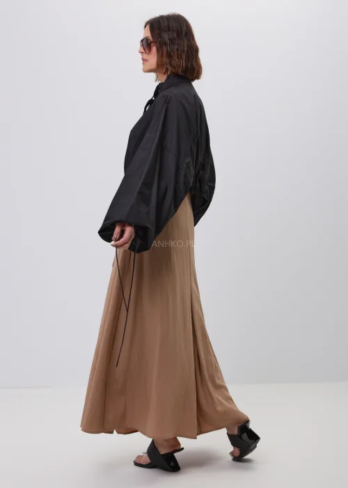 Czarna damska kurtka bomber oversize ze stójką, szerokimi rękawami i regulowanymi troczkami przy mankietach. Nowoczeska stylizacja casual z krótką kurtką i beżową spódnicą maxi.