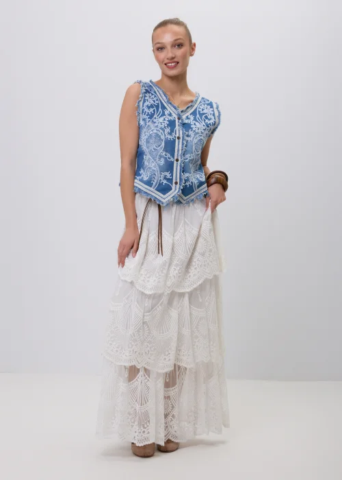 Niebieska jeansowa kamizelka damska z ozdobnym białym haftem i postrzępionym wykończeniem. Model zapinany na guziki, inspirowany stylem boho i vintage, zestawiony z koronkową spódnicą maxi w eleganckiej stylizacji.
