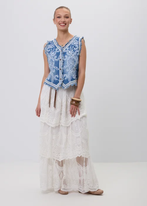 Niebieska jeansowa kamizelka damska z ozdobnym białym haftem i postrzępionym wykończeniem. Model zapinany na guziki, inspirowany stylem boho i vintage, zestawiony z koronkową spódnicą maxi w eleganckiej stylizacji.