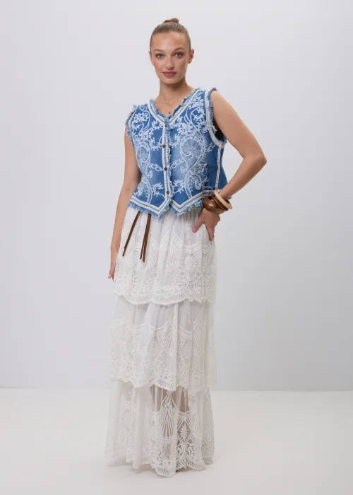 Biała koronkowa spódnica maxi w stylu boho z warstwowymi falbanami, ażurowymi haftami i ozdobnym brązowym paskiem w talii. Romantyczny model o efektownym wykończeniu, idealny do letnich i eleganckich stylizacji.