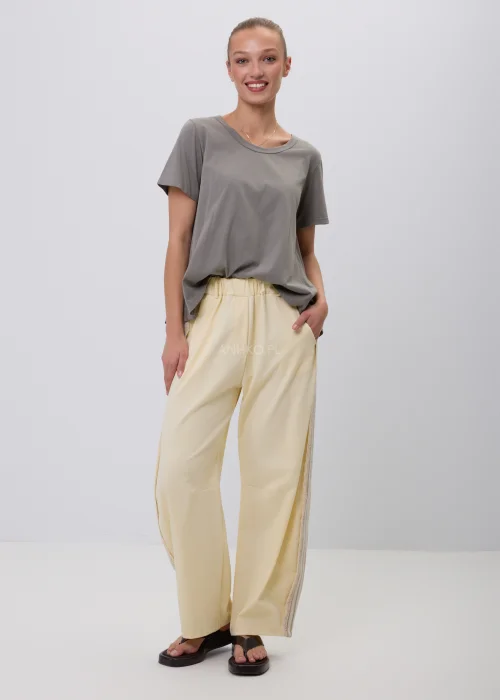 Szary damski T-shirt oversize o luźnym, lekko rozkloszowanym fasonie z krótkim rękawem i okrągłym dekoltem. Minimalistyczna bluzka basic w stonowanym odcieniu, zestawiona z jasnymi spodniami w eleganckiej codziennej stylizacji.
