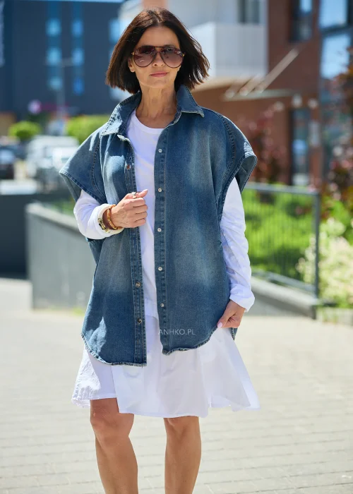 Jeansowa kamizelka oversize damska z efektem sprania, zapinana na napy, z szerokimi rękawami i wysokim kołnierzem. Model stylizowany z białą sukienką, tworzący nowoczesny casualowy look.