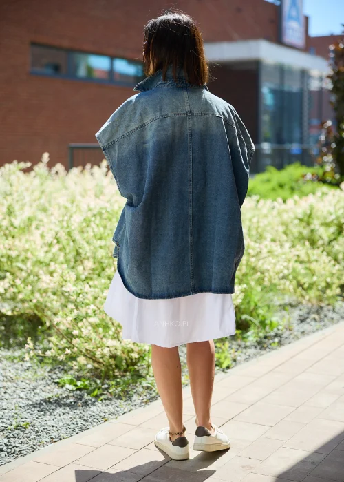 Jeansowa kamizelka oversize damska z efektem sprania, zapinana na napy, z szerokimi rękawami i wysokim kołnierzem. Model stylizowany z białą sukienką, tworzący nowoczesny casualowy look.