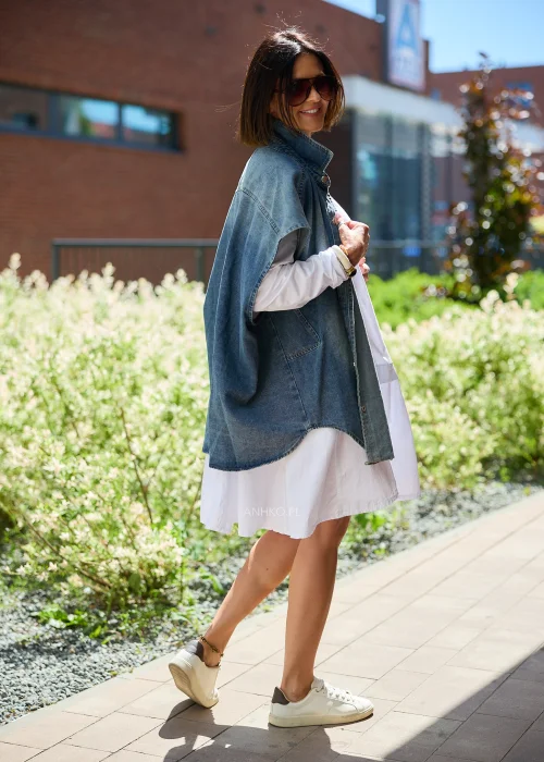 Jeansowa kamizelka oversize damska z efektem sprania, zapinana na napy, z szerokimi rękawami i wysokim kołnierzem. Model stylizowany z białą sukienką, tworzący nowoczesny casualowy look.