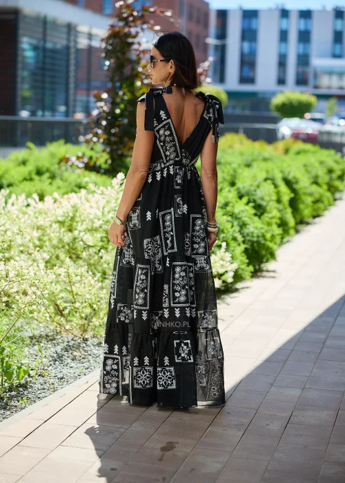 Czarna sukienka maxi damska z białym etnicznym wzorem, kopertowym dekoltem i wiązanymi ramiączkami. Zwiewny model boho z falbaną u dołu, idealny do letnich i wakacyjnych stylizacji.