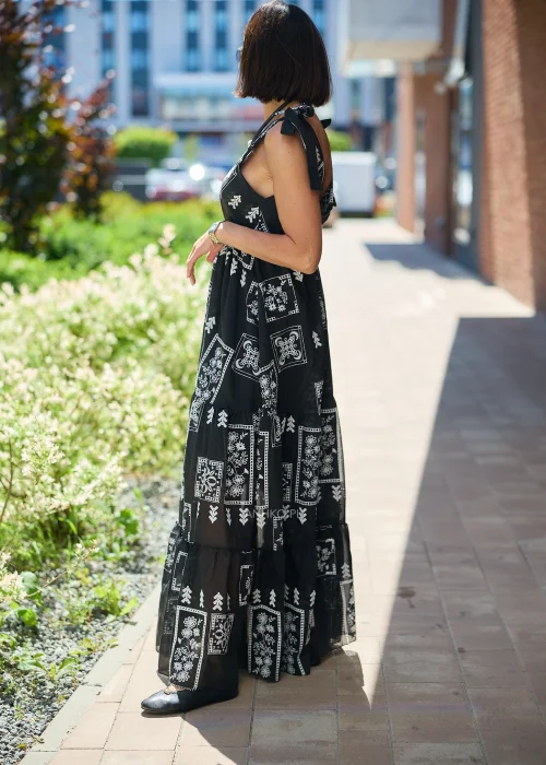Czarna sukienka maxi damska z białym etnicznym wzorem, kopertowym dekoltem i wiązanymi ramiączkami. Zwiewny model boho z falbaną u dołu, idealny do letnich i wakacyjnych stylizacji.