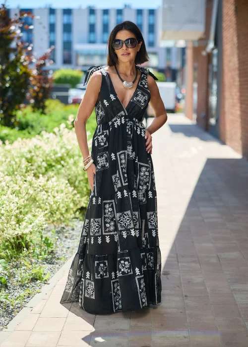 Czarna sukienka maxi damska z białym etnicznym wzorem, kopertowym dekoltem i wiązanymi ramiączkami. Zwiewny model boho z falbaną u dołu, idealny do letnich i wakacyjnych stylizacji.