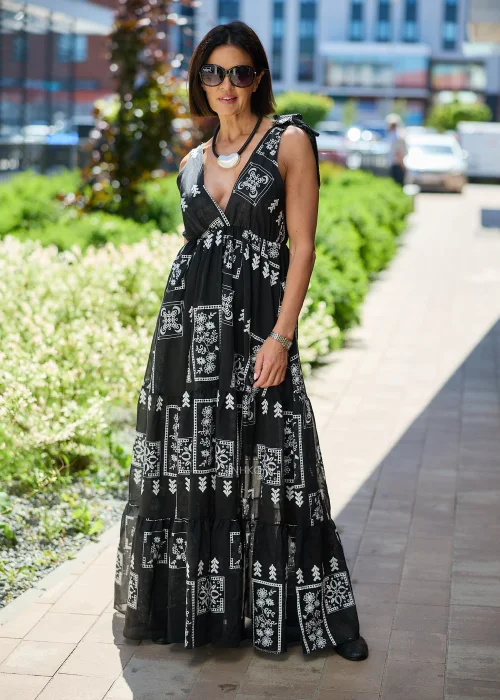 Czarna sukienka maxi damska z białym etnicznym wzorem, kopertowym dekoltem i wiązanymi ramiączkami. Zwiewny model boho z falbaną u dołu, idealny do letnich i wakacyjnych stylizacji.