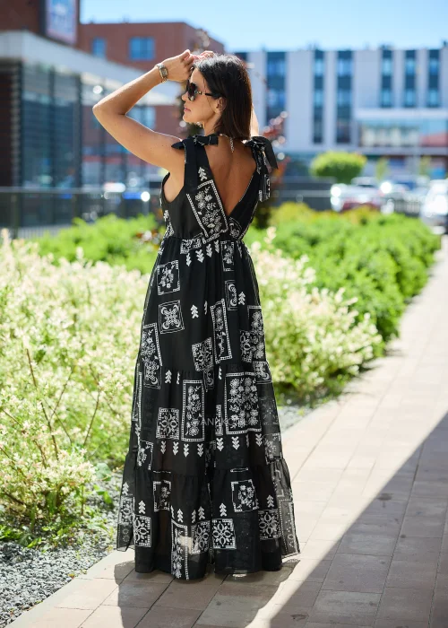 Czarna sukienka maxi damska z białym etnicznym wzorem, kopertowym dekoltem i wiązanymi ramiączkami. Zwiewny model boho z falbaną u dołu, idealny do letnich i wakacyjnych stylizacji.