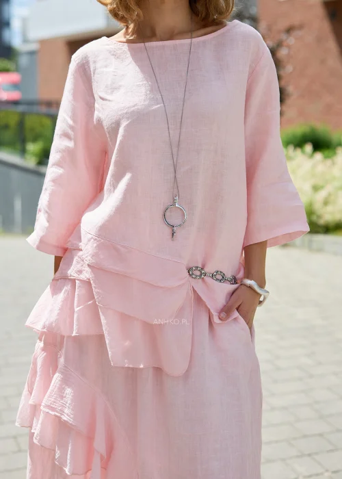 Pudroworóżowa lniana bluzka damska z rękawem 3/4, asymetrycznymi falbanami i luźnym fasonem oversize, prezentowana w eleganckiej miejskiej stylizacji.