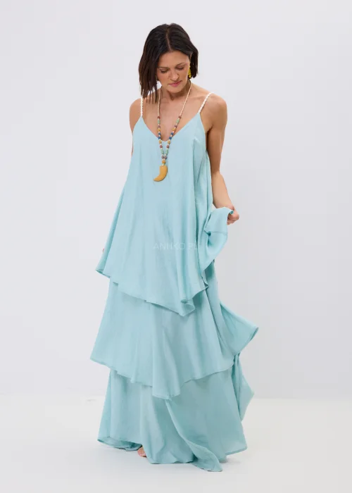 Błękitna sukienka maxi damska na cienkich ramiączkach z ozdobnym splotem, o luźnym fasonie i wielowarstwowych falbanach. Zwiewny model w stylu boho uzupełniony kolorowym naszyjnikiem i letnimi dodatkami.