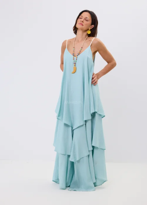 Błękitna sukienka maxi damska na cienkich ramiączkach z ozdobnym splotem, o luźnym fasonie i wielowarstwowych falbanach. Zwiewny model w stylu boho uzupełniony kolorowym naszyjnikiem i letnimi dodatkami.