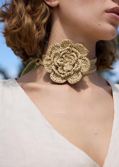 Pleciony dodatek z rafii w naturalnym beżowym odcieniu z dużym kwiatem, który można nosić jako naszyjnik lub pasek. Wielofunkcyjny model w stylu boho efektownie uzupełnia sukienki, tuniki i letnie stylizacje.